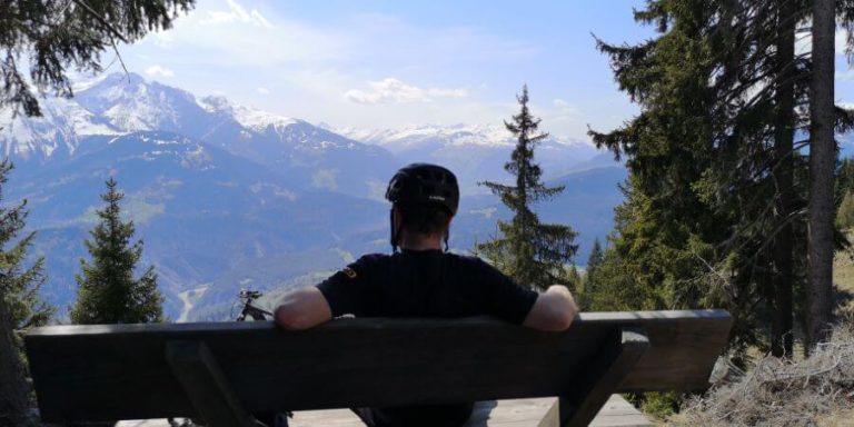 Mountainbiker sitzt auf einer Bank und schaut in die Berge