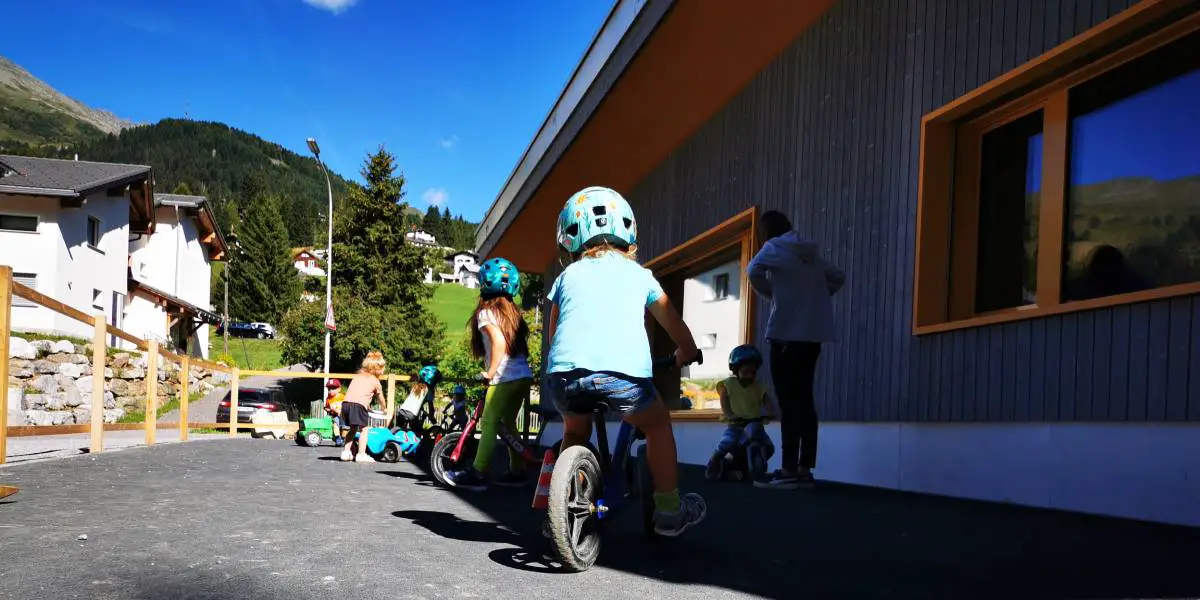 Kinder der Kinderkrippe Purzelbaum in Valbella fahren mit ihren Laufrädern auf dem Vorplatz der Krippe herum.